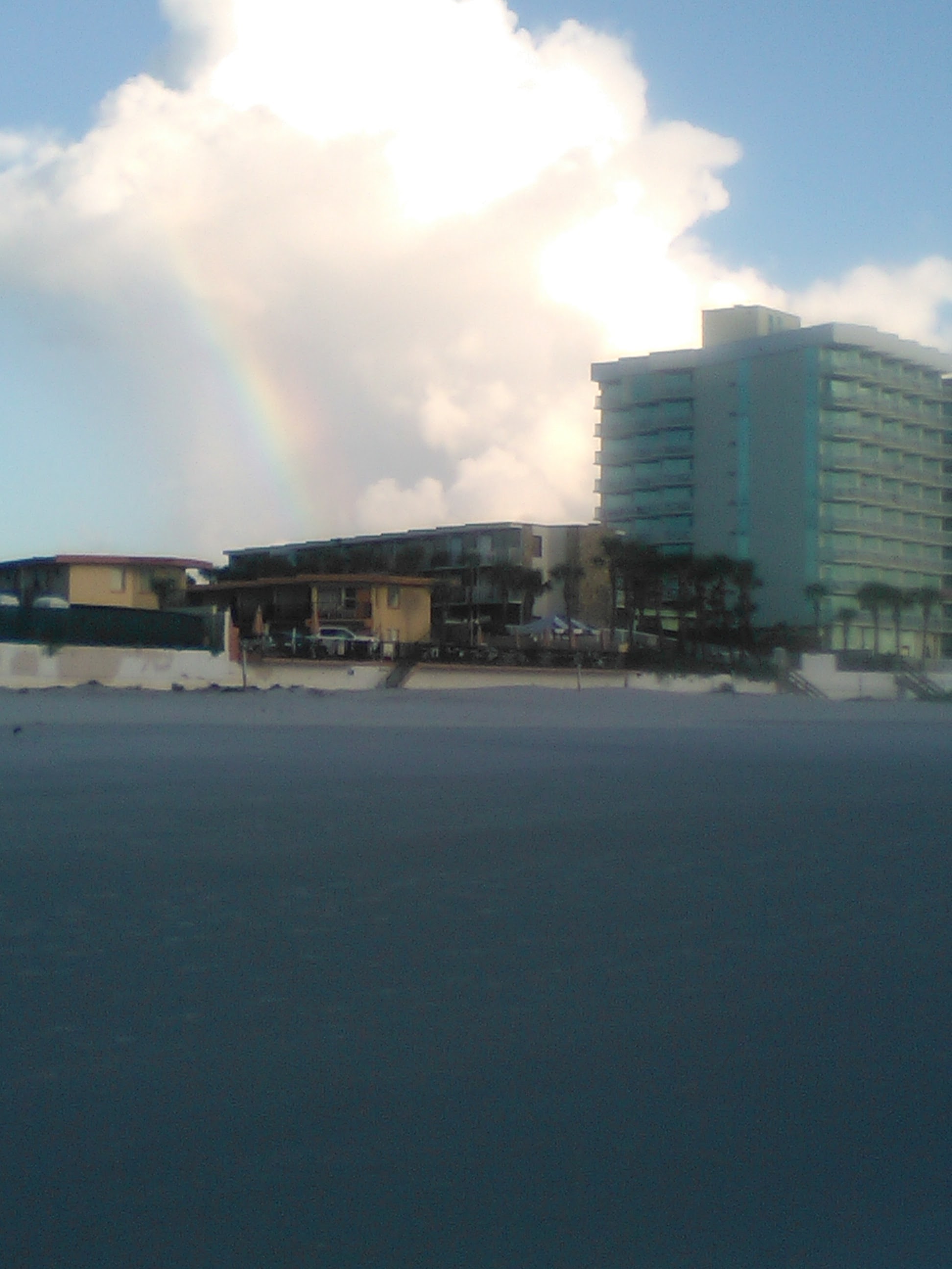 Rainbow coming from a cloud over buildings on a beach.